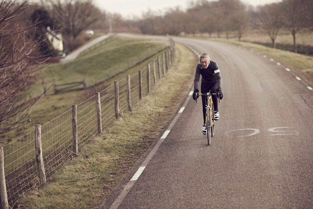 Nederlandse Wielerfotografie 'Windswept' - Albert, een 82-jarige wielrenner, op zijn op maat gebouwde stalen fiets langs de Waal- en Lekdijken, Nederland, fine art print door Cyclingprints.nl