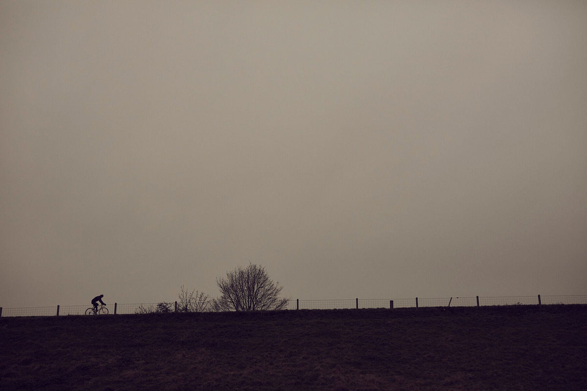 Nederlandse Wielerfotografie 'Wintry Dikes' - Albert, een 82-jarige wielrenner, op zijn op maat gebouwde stalen fiets langs de Waal- en Lekdijken, Nederland, fine art print door Cyclingprints.nl
